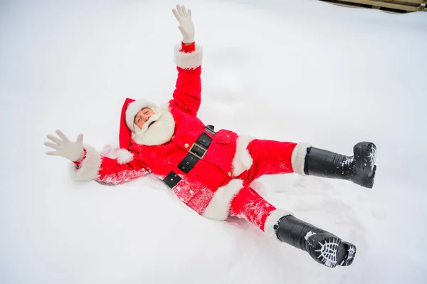 Щасливий Санта Клаус лежить на снігу і обманює навколо — стокове фото