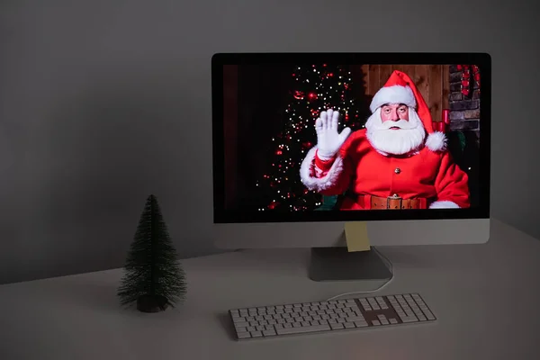 Санта Клаус віддалено бажає Веселого Різдва за допомогою відеодзвінка на комп'ютері. Людина, одягнена як Санта Клаус на моніторі. 2021 рік. — стокове фото