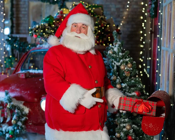 Santa Claus posílá dárek poštou. Muž oblečený jako Santa vloží vyzdobenou krabici do schránky — Stock fotografie