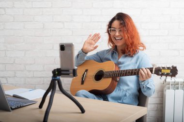 Beyaz bir kadın akıllı bir telefondan gitar çalıyor. Kız bir müzik videosu blogu yönetiyor.