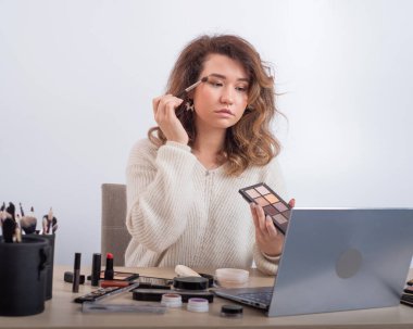 Beyaz bir kadın akıllı telefondan çevrimiçi makyaj eğitiminin videosunu kaydediyor. Video blogcusu kız göz farı sürüyor