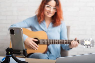 Çekici kızıl saçlı bir kadın müzik hakkında blog yazıyor. Kız şarkı söylüyor, gitar çalıyor ve akıllı telefondan video kaydediyor.