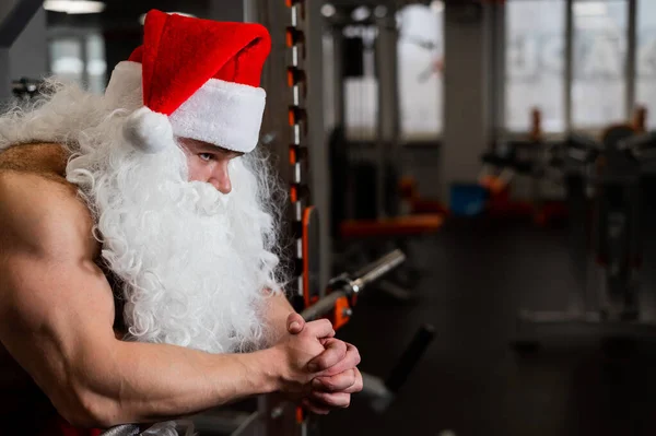 Mężczyzna w czapce Świętego Mikołaja i nagim tułowiu pozowanie na siłowni. — Zdjęcie stockowe
