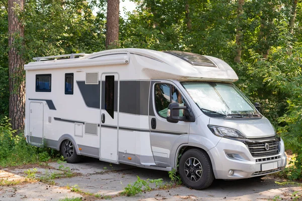 A white mobile home is parked in the woods. Caravan for life and family road travel. No people.