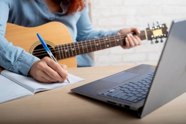 Gitarlı bir kadın deftere notlar yazar. Kız bir şarkı yazıyor.