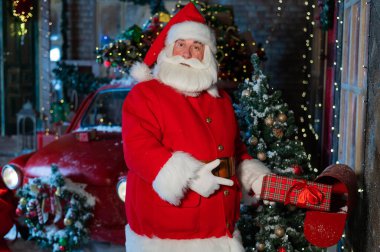 Noel Baba postayla bir hediye gönderir. Noel Baba gibi giyinmiş bir adam süslü bir kutuyu posta kutusuna koyar.