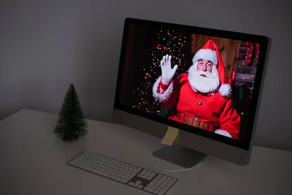 Święty Mikołaj zdalnie życzy Wesołych Świąt za pośrednictwem połączenia wideo na komputerze. Mężczyzna przebrany za Świętego Mikołaja na monitorze. Koncepcja nowego roku 2021 — Zdjęcie stockowe