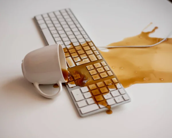 Café preto derramado em um teclado de computador em uma mesa branca — Fotografia de Stock