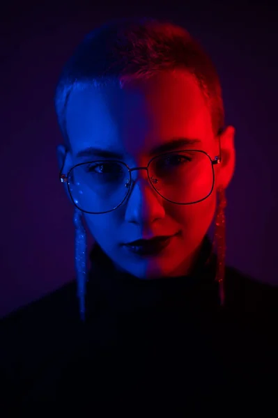 Nahaufnahme Porträt einer jungen blonden Frau mit kurzen Haaren, die eine Brille im Neonlicht trägt — Stockfoto