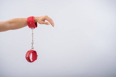 Beyaz arka planda kırmızı deri kelepçeler ve kadın elleri. BDSM aksesuarları