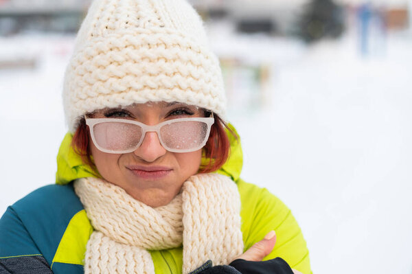 Portrait of a woman in glasses covered with hoarfrost. Upset girl freezing in very cold weather outdoors.