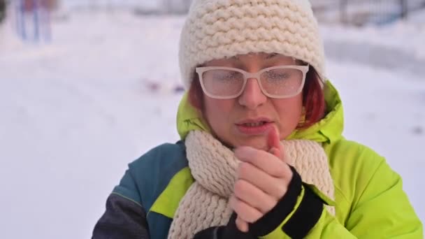 Portret van een vrouw met een bril bedekt met ijzel. Het meisje is ijskoud en vergat handschoenen bij zeer koud weer en blaast op haar blote handen — Stockvideo