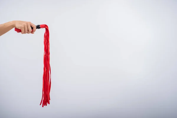 Rote Lederpeitsche in Frauenhand auf weißem Hintergrund. Kopierraum. — Stockfoto