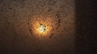 Gün batımında donmuş bir kış penceresinde çizilmiş bir kalp..