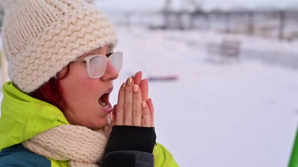 Portret van een vrouw met een bril bedekt met ijzel. Het meisje is ijskoud en vergat handschoenen bij zeer koud weer en blaast op haar blote handen — Stockvideo