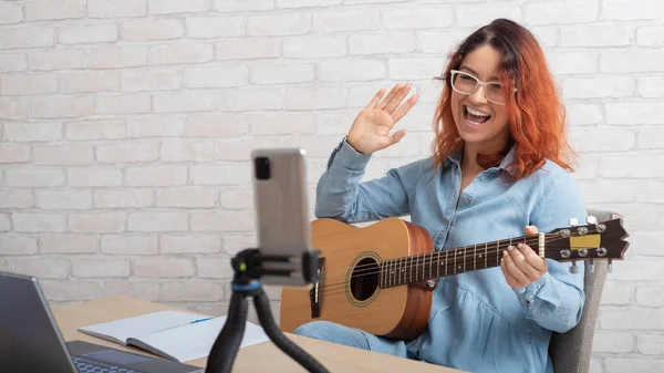 스마트폰으로 기타를 연주하는 백인 여성. 그는 뮤직 비디오 블로그를 이끌고 있다. — 스톡 사진
