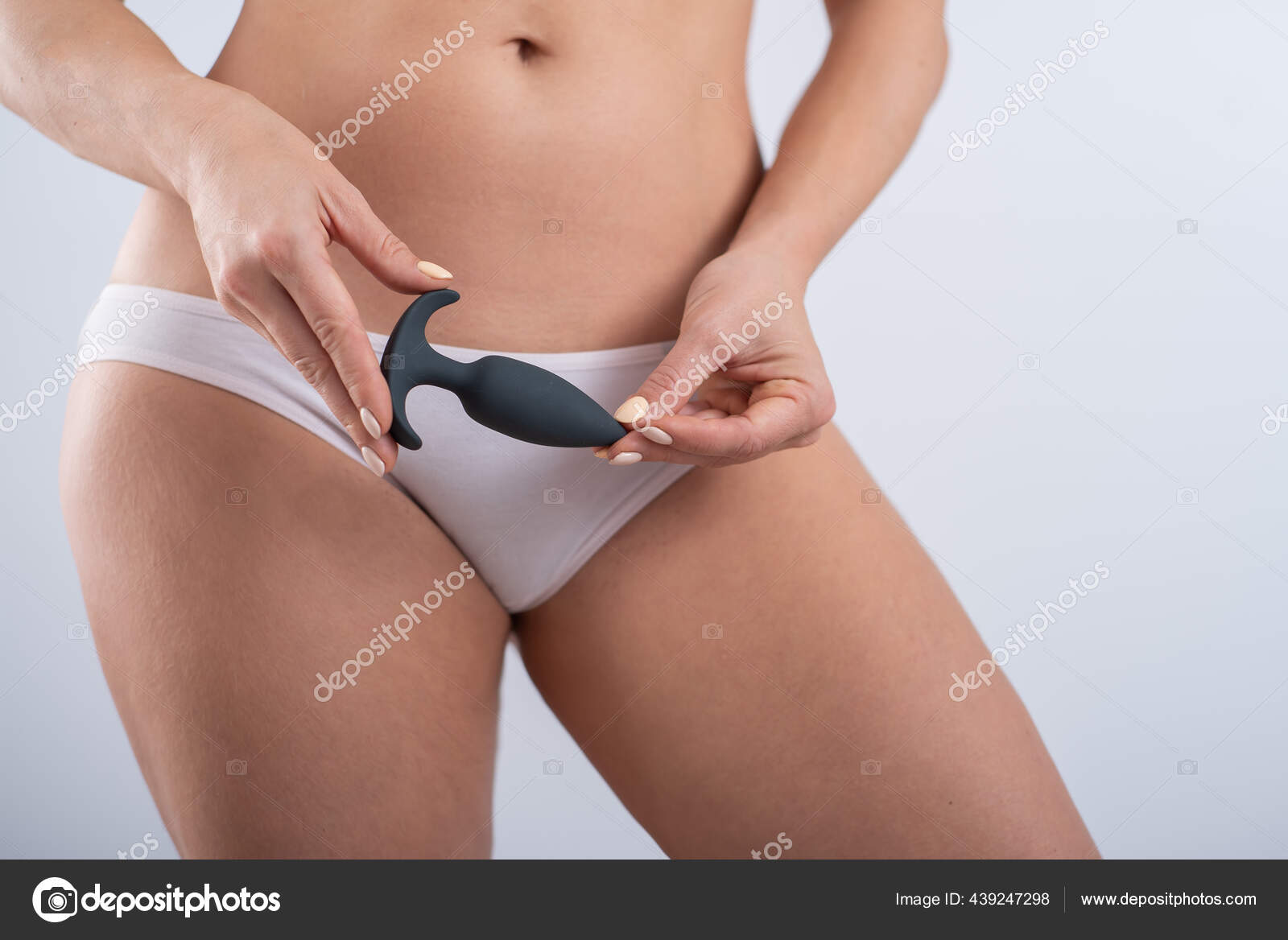 A faceless woman in white cotton panties holds a black butt plug