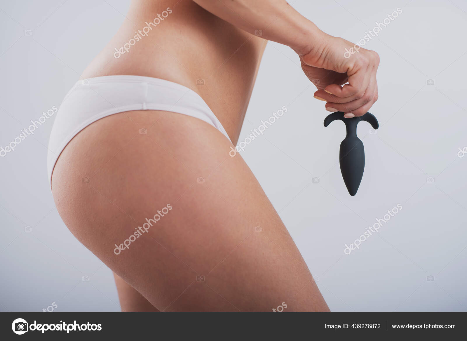 A faceless woman in white cotton panties holds a black butt plug