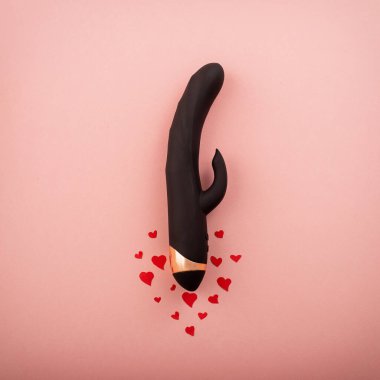 Black clitoral vaginal dildo and hearts on a pink background. Female vibrator as a gift for Valentines Day