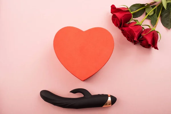 Чорний кліторальний вагінальний фалоімітатор і коробка у формі серця і червоні троянди на рожевому фоні. Еротичний подарунок на день валентинки — стокове фото