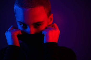 Yüzünde neon ışıklı balıkçı yaka kazak olan kısa saçlı kadının portresi..