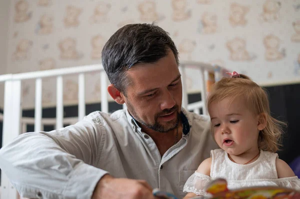 Доглянутий батько читає казку своїй маленькій доньці в дитячій спальні . — стокове фото