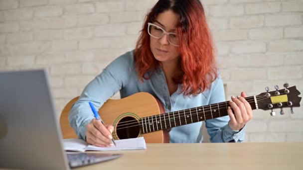 Μια γυναίκα με κιθάρα γράφει σημειώσεις σε ένα σημειωματάριο. Το κορίτσι συνθέτει ένα τραγούδι. — Αρχείο Βίντεο