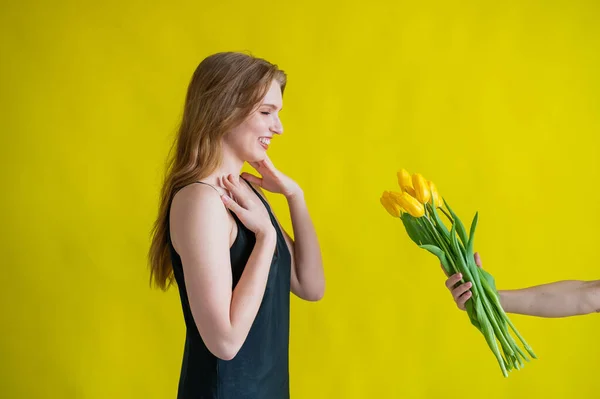 Caucasian woman accepts tulips as a gift on yellow background. — Stock Photo, Image