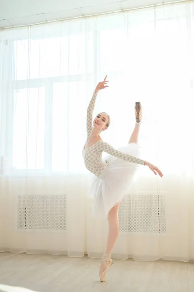 Hermosa bailarina en cuerpo y tutú blanco está entrenando en una clase de baile. Joven bailarina flexible posando en zapatos puntiagudos. —  Fotos de Stock