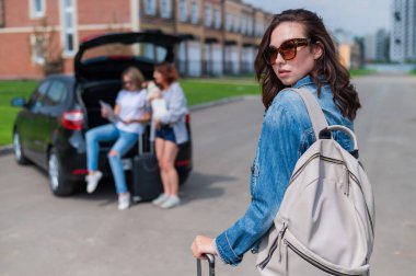 Üç kız arkadaş bir yolculuğa çıkıyor. Elinde bavulla poz veren genç bir kadın. İki kız bir arabanın bagajında oturmuş haritayı izliyorlar..