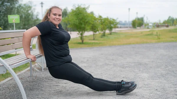 Junge dicke Frau macht Liegestütze von der Bank im Freien. Molliges Mädchen macht Fitnessübungen. — Stockfoto