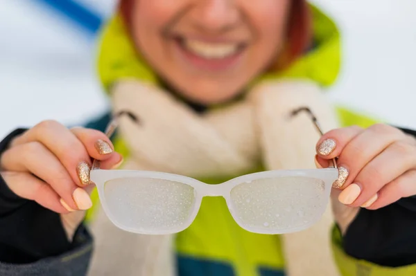 Lächelnde Kaukasierin nimmt im Winter im Freien gefrorene Gläser ab. Das Mädchen ist kalt. — Stockfoto