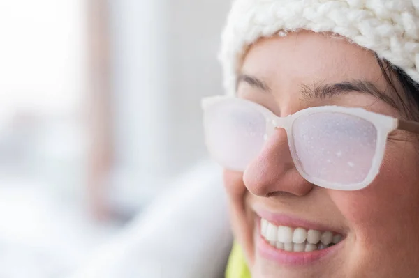 Mulher branca sorridente fica na varanda de uma casa de tijolos no inverno. Menina feliz em óculos cobertos de gelo na rua ao ar livre — Fotografia de Stock
