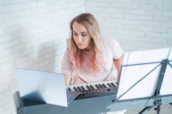 Een vriendelijke vrouw speelt elektronische piano en dirigeert een videoblog op haar laptop. Blijf thuis. Muziekinstrumentenleraar. Muziek voor afstandsonderwijs in quarantaine. — Stockfoto
