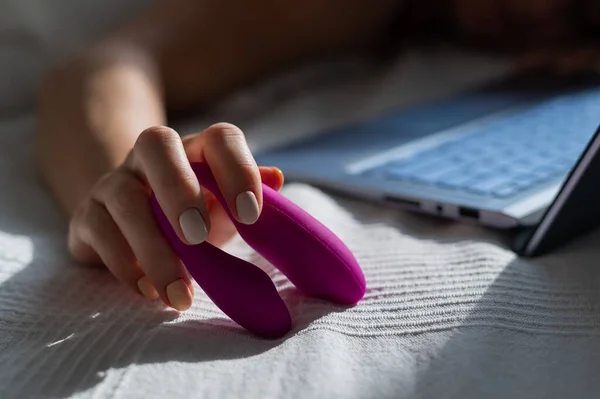 Женщина лежит в постели с вибратором клитора и смотрит порно на ноутбуке. Девушка занимается сексом онлайн — стоковое фото