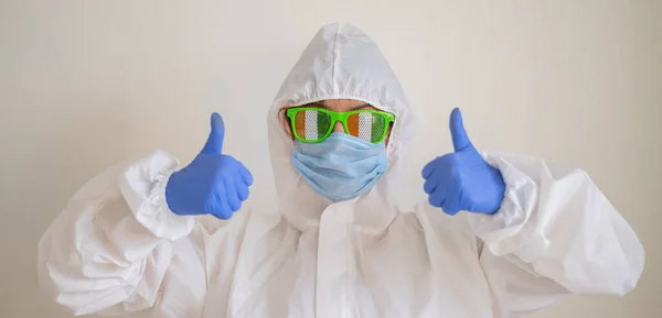 Una mujer con un traje protector y una máscara médica y con gafas divertidas celebra el día de San Patricio y muestra un pulgar hacia arriba — Foto de Stock