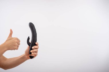 Faceless woman holding black dildo with clitoris stimulator on white background