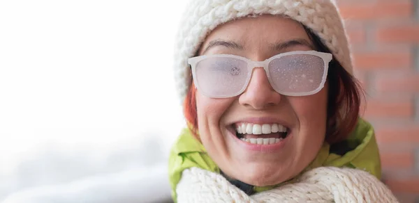 Lächelnde Kaukasierin steht im Winter auf dem Balkon eines Backsteinhauses. Glückliches Mädchen in eisbedeckter Brille auf der Straße im Freien — Stockfoto