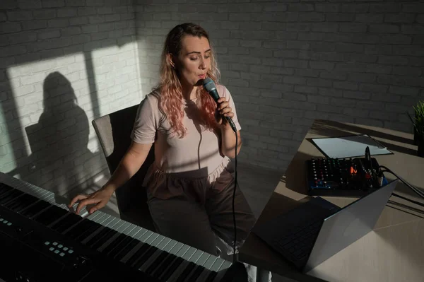 A female blogger sings and plays the live electronic piano. Portrait of a girl recording a song on a web camera and composing on a synthesizer. Online music lessons. Distance learning in quarantine.
