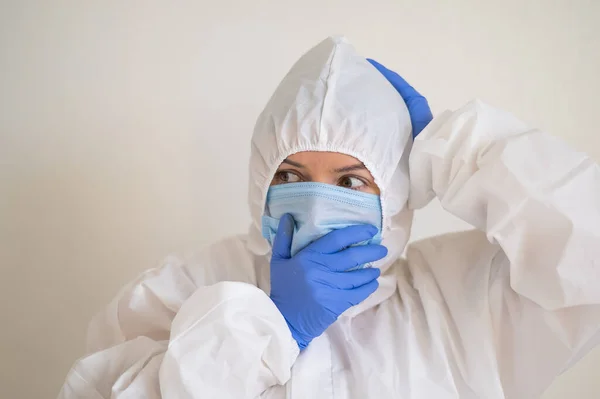 Frightened woman in a protective suit, mask and gloves holds her head. Fear in the eyes of a virologist doctor — Stock Photo, Image