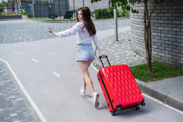 Mulher caucasiana bonita feliz está correndo com uma grande mala vermelha ao ar livre. Garota excitada está atrasada para o avião. — Fotografia de Stock