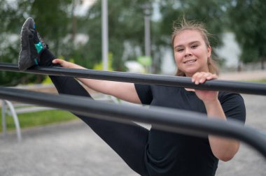 Şişman kız oyun parkındaki dengesiz parmaklıkların üzerinde gerinmekle meşgul. Kilo vermek için spor yapan güzel, genç, güler yüzlü bir kadın..