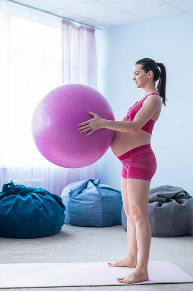 Těhotná žena ve sportovním oblečení dělá gymnastiku pro těhotné ženy. Dívka je zapojena do fitness s míčem pro nastávající matky. Poslední trimestr. — Stock fotografie