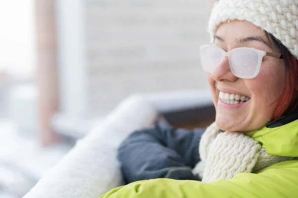 Lächelnde Kaukasierin steht im Winter auf dem Balkon eines Backsteinhauses. Glückliches Mädchen in eisbedeckter Brille auf der Straße im Freien — Stockfoto