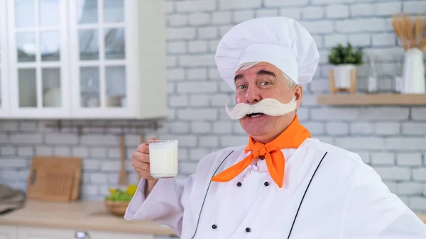 A friendly elderly milkman with a glass of milk. Portrait of a male farmer with a bushy mustache.