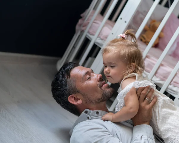Кавказький чоловік лежить на спині і тримає свою дочку над собою у дитячій кімнаті. — стокове фото