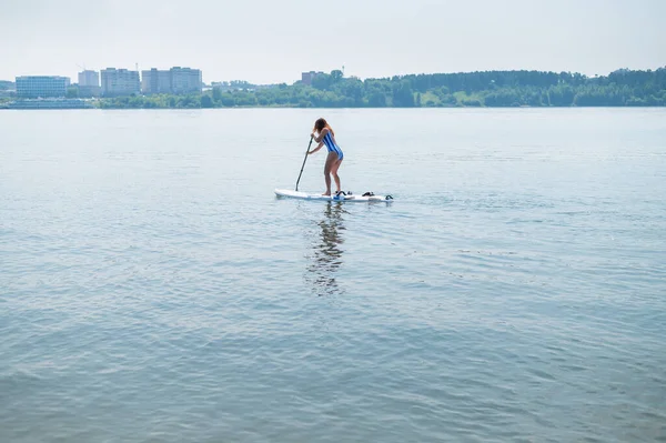 Mulher caucasiana em um maiô listrado cavalga em um SUP board. A menina prefere o resto ativo. — Fotografia de Stock