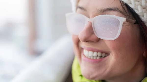 Glimlachende blanke vrouw staat in de winter op het balkon van een stenen huis. gelukkig meisje in ijs bedekte glazen op de straat buiten — Stockfoto