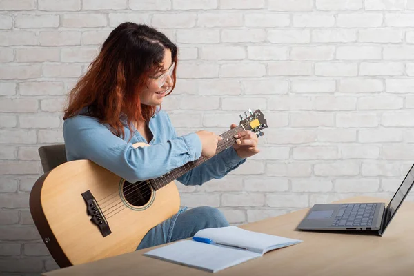 Kaukasierin unterrichtet aus der Ferne am Laptop das Gitarrespielen. Online-Musikschulung — Stockfoto