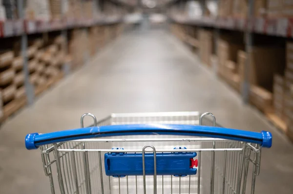 Carrinho de compras vazio em um armazém de loja de móveis. Supermercado shopping cesta corredor com caixa prateleira abstrato borrão desfocado fundo — Fotografia de Stock